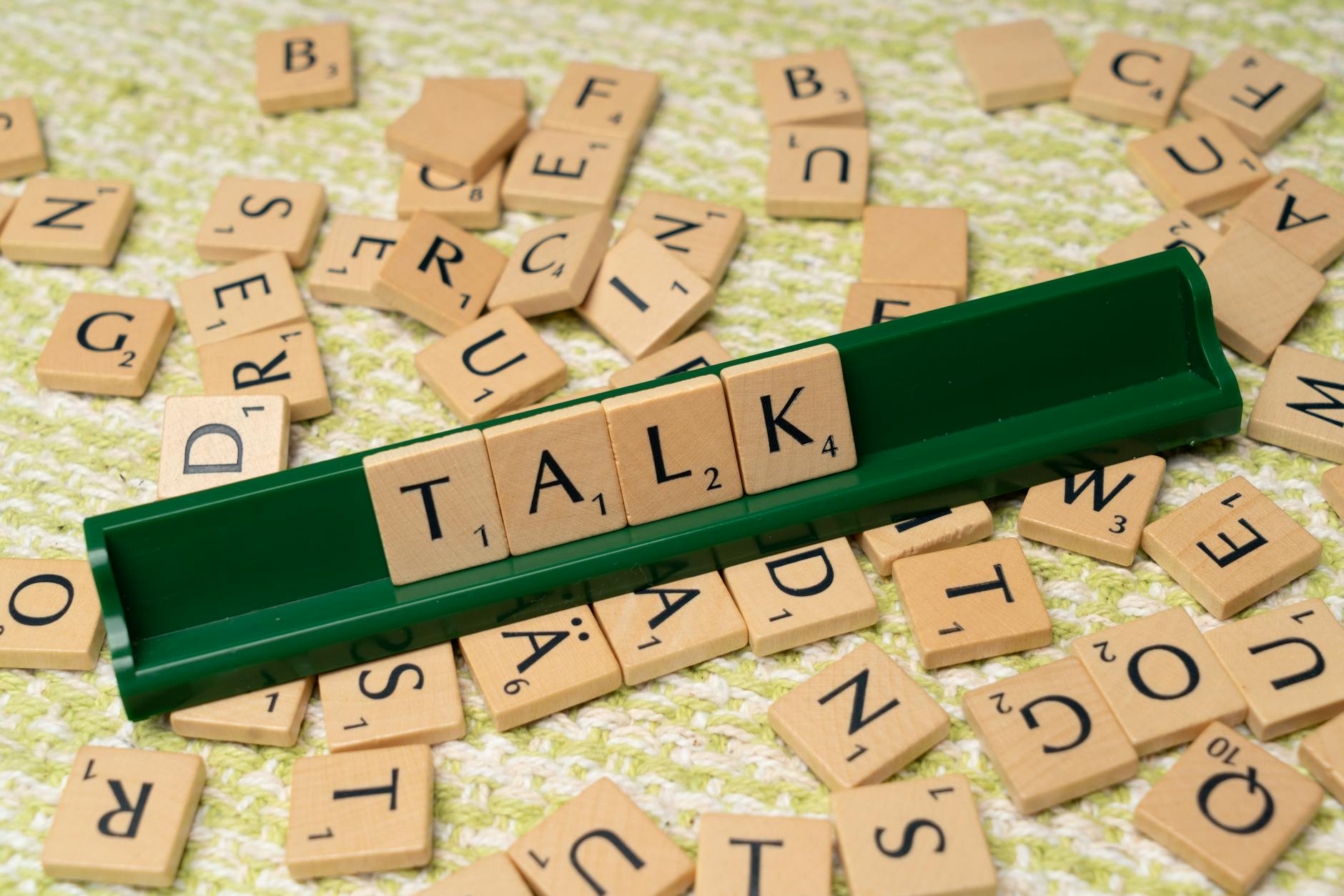 Logopedyczne gry planszowe i aplikacje, które warto znać i mądrze używać Kafle Scrabble układające słowo TALK na zielonej podstawce